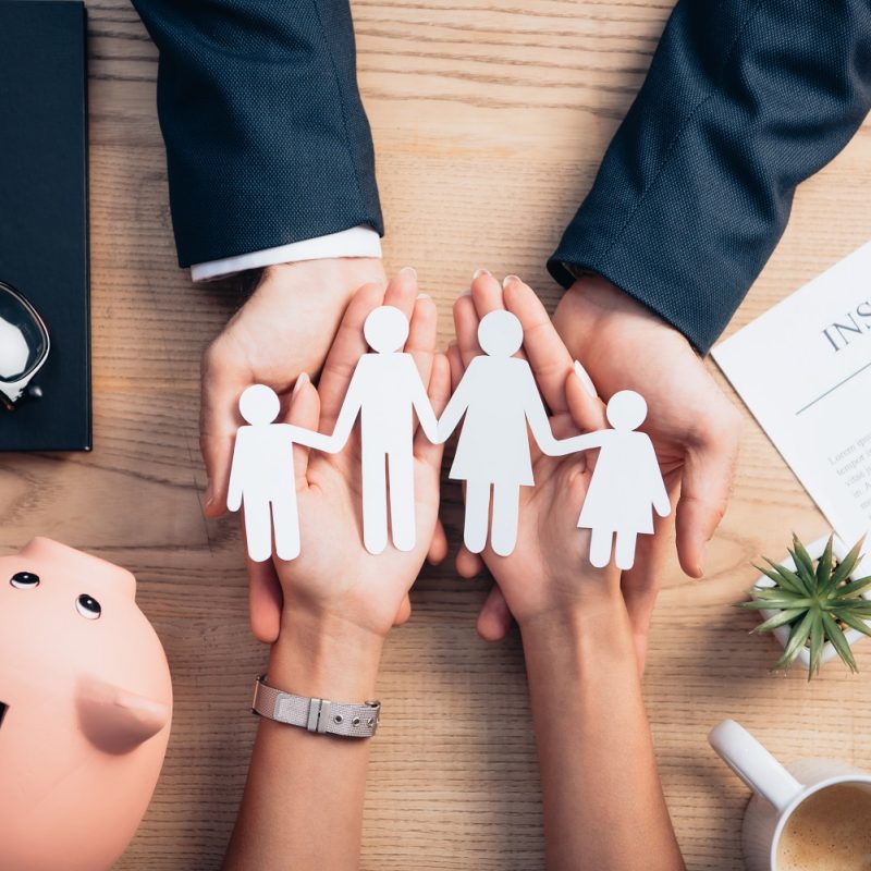 top view of lawyer and woman holding paper cut family near cup of coffee, insurance policy